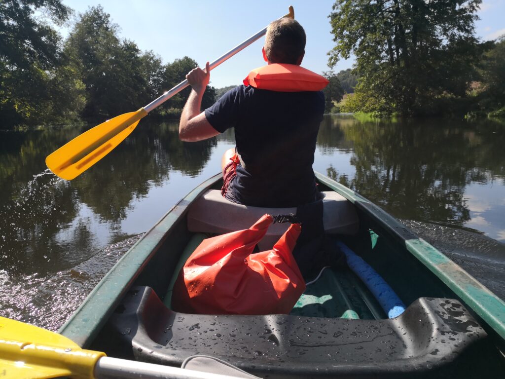 Blick über die Schulter eines Paddlers in einem Kanu auf einem ruhigen Fluss, Betriebsausflug auf der Naab