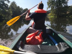 Blick über die Schulter eines Paddlers in einem Kanu auf einem ruhigen Fluss, Betriebsausflug auf der Naab