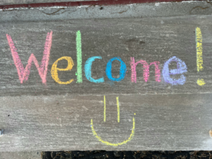 Mit Kreide auf eine Steinplatte geschriebenes „Welcome!“ mit Smiley