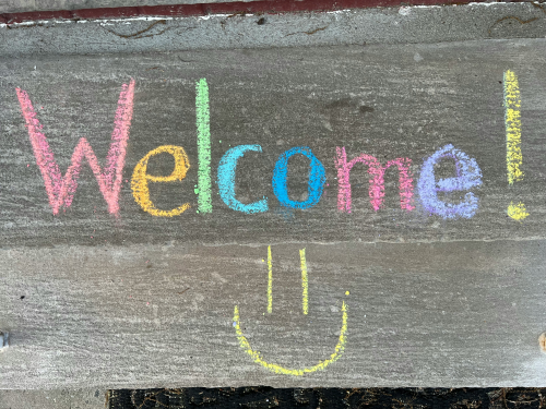Mit Kreide auf eine Steinplatte geschriebenes „Welcome!“ mit Smiley