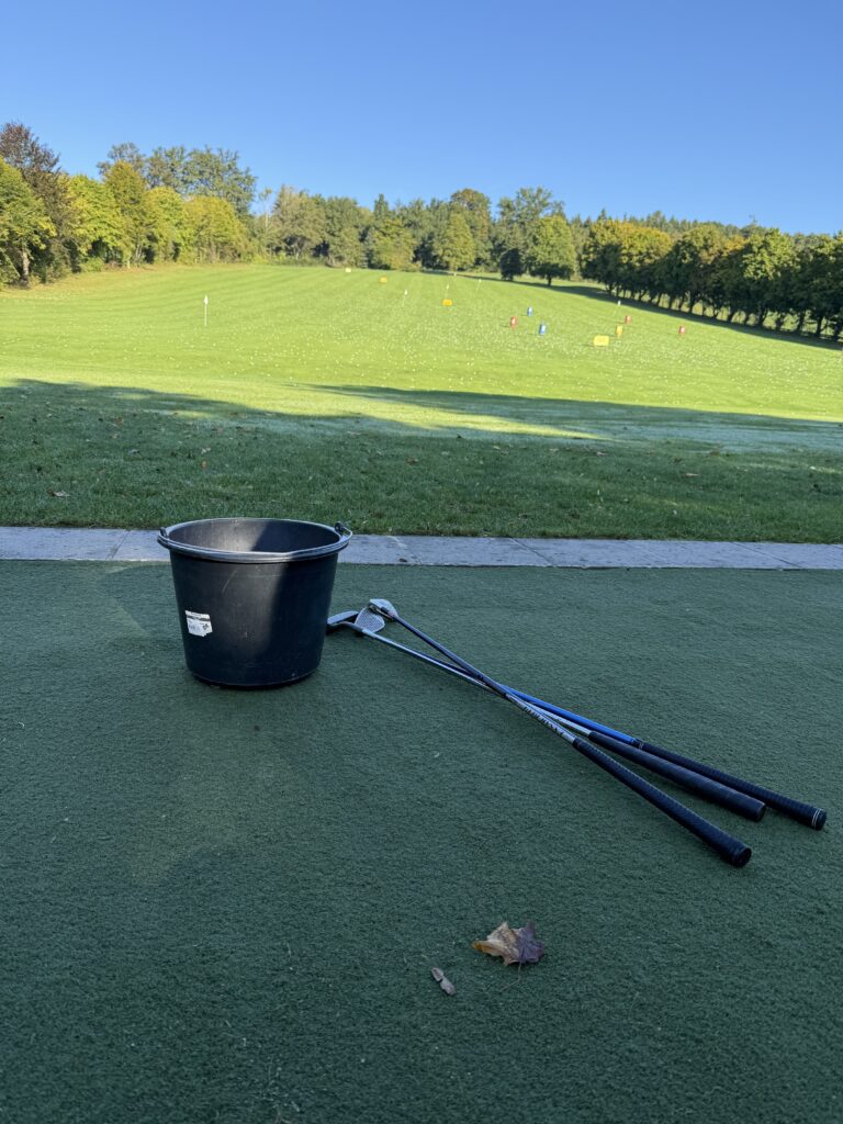 Eimer und Golfschläger auf einer Abschlagsmatte vor einer Wiese