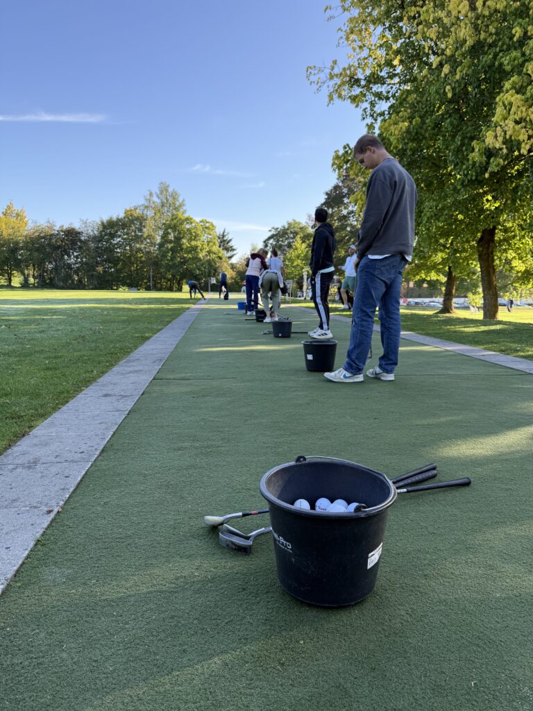 Golf-Übungsanlage mit mehreren Personen und einem Eimer Golfbälle
