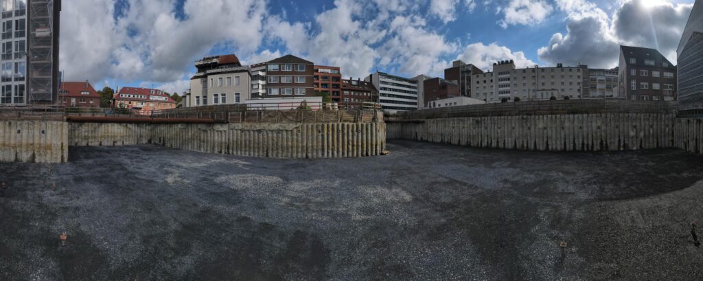 Panorama der Baugrubensohle mit umlaufender Bohrpfahlwand und Häusern dahinter