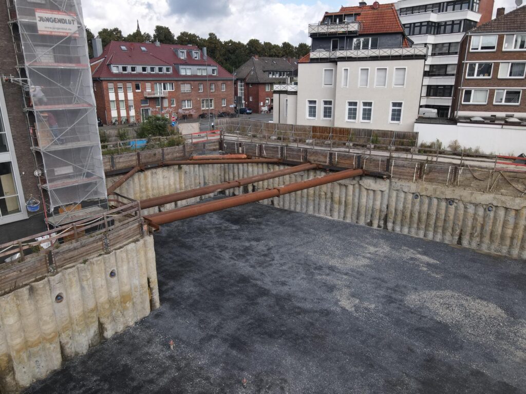 Baugrube mit Stahlsteifen an der Ecke zwischen Bohrpfahlwand und Nachbarbebauung