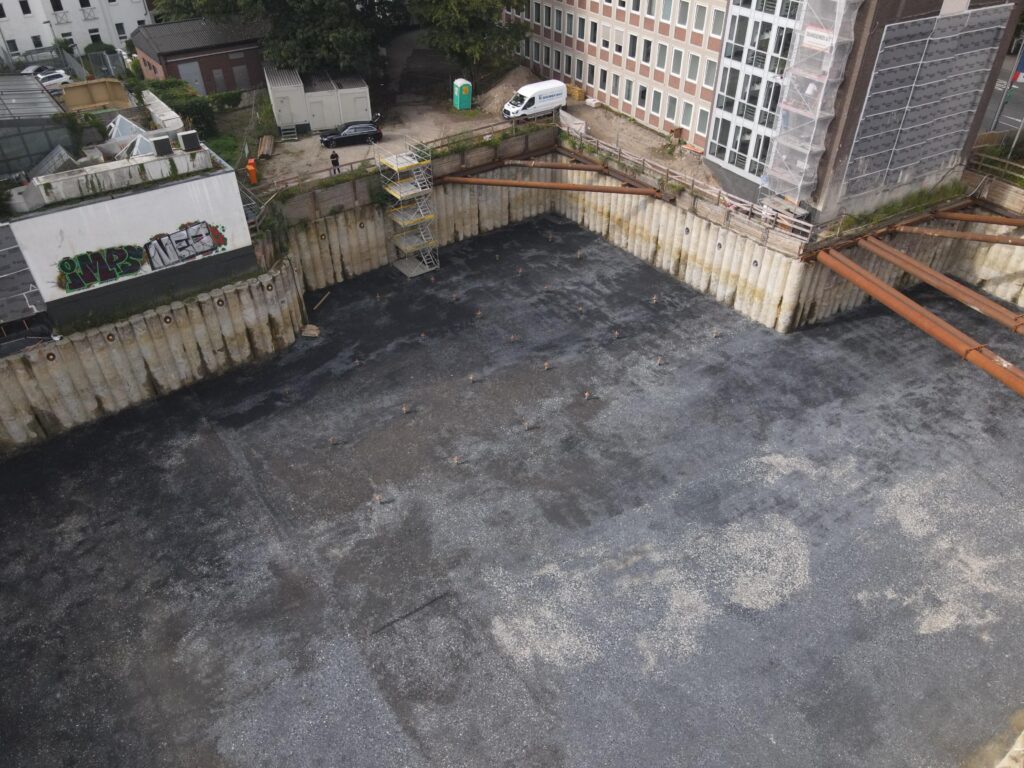 Ecke der Baugrube mit Stahlaussteifung vor einem mehrgeschossigen Bürogebäude
