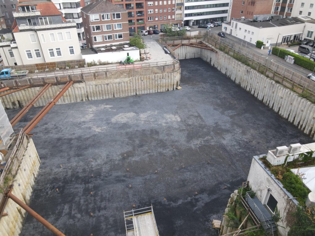 Blick von oben in die ausgehobene Baugrube in Münster mit Bohrpfahlwänden und Stahlaussteifung, ringsum dichte Bebauung