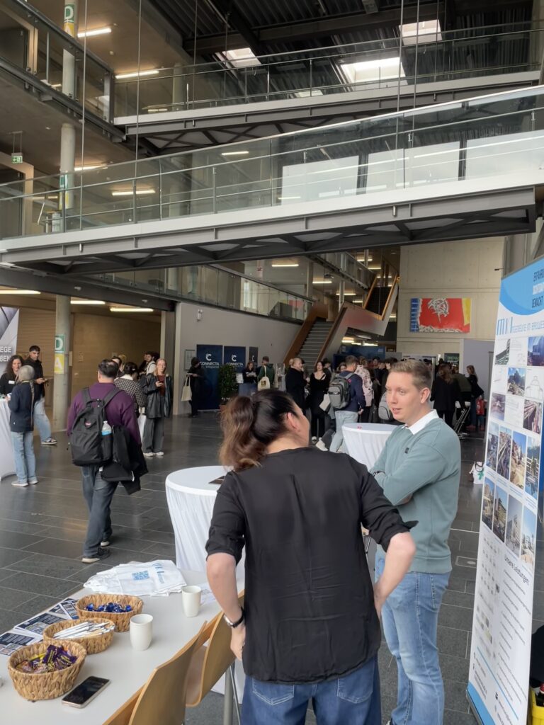 Studierende im Gespräch am MKI-Messestand, im Hintergrund die Halle mit weiteren Besuchern